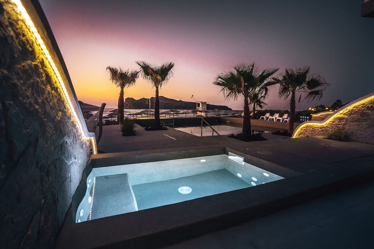 A pool area with a view of the ocean and palm trees at dusk.