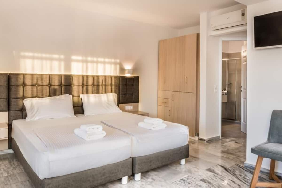 A modern hotel room with a large bed, a wardrobe, a seating area, and a TV on the wall.