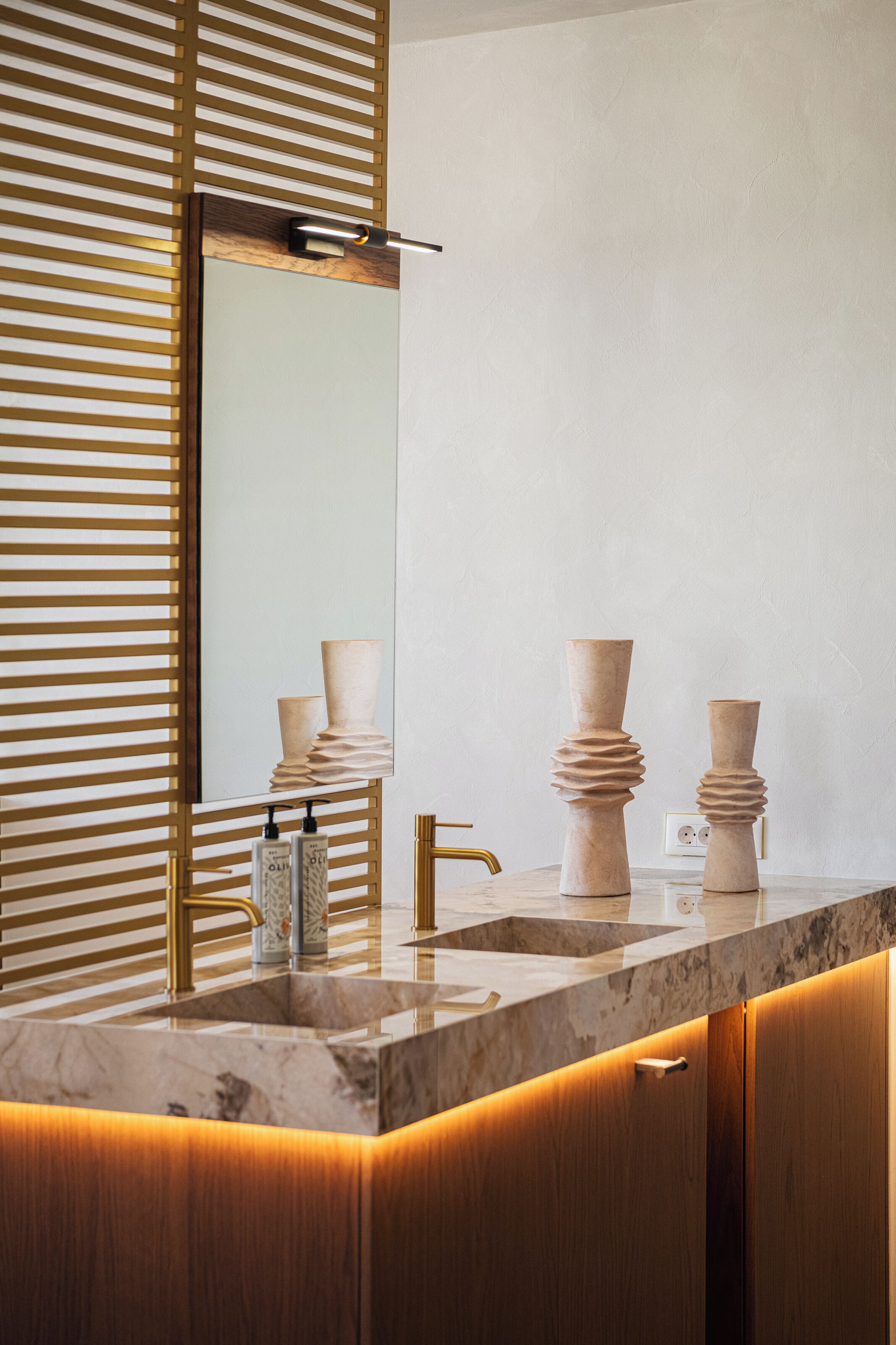Un baño moderno con lavamanos de mármol, grifería dorada y listones de madera.