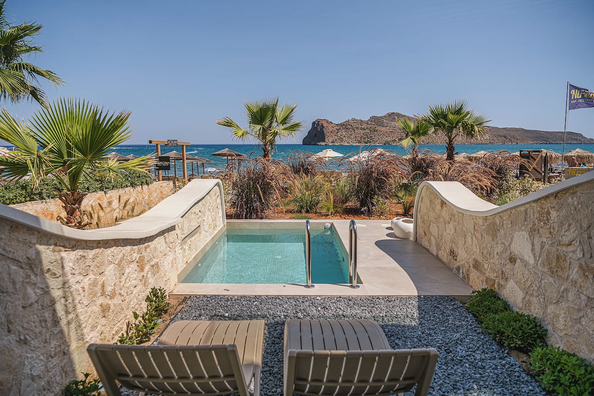 A pool area with a view of the sea, surrounded by palm trees and lounge chairs.