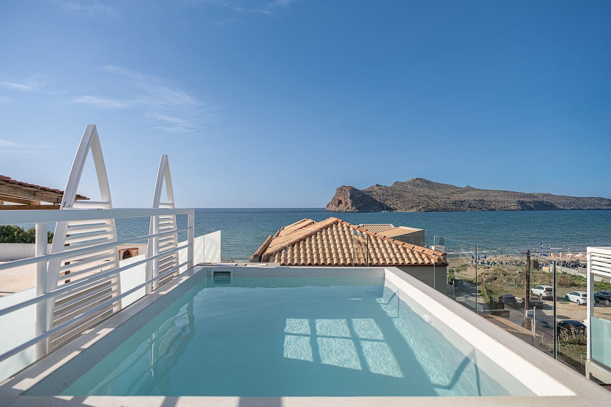A rooftop infinity pool with a clear view of the sea and a rocky island in the distance.