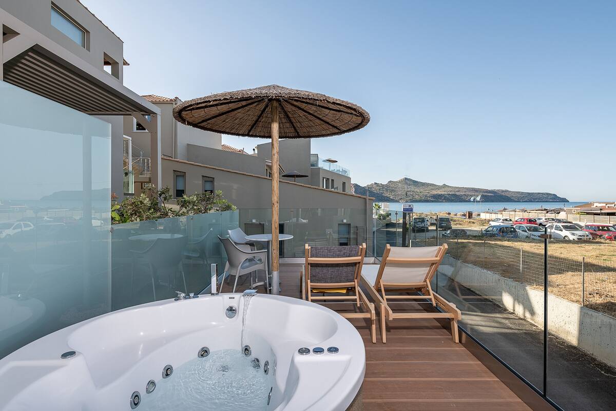 A modern outdoor balcony with a hot tub, seating area, and a view of the sea.