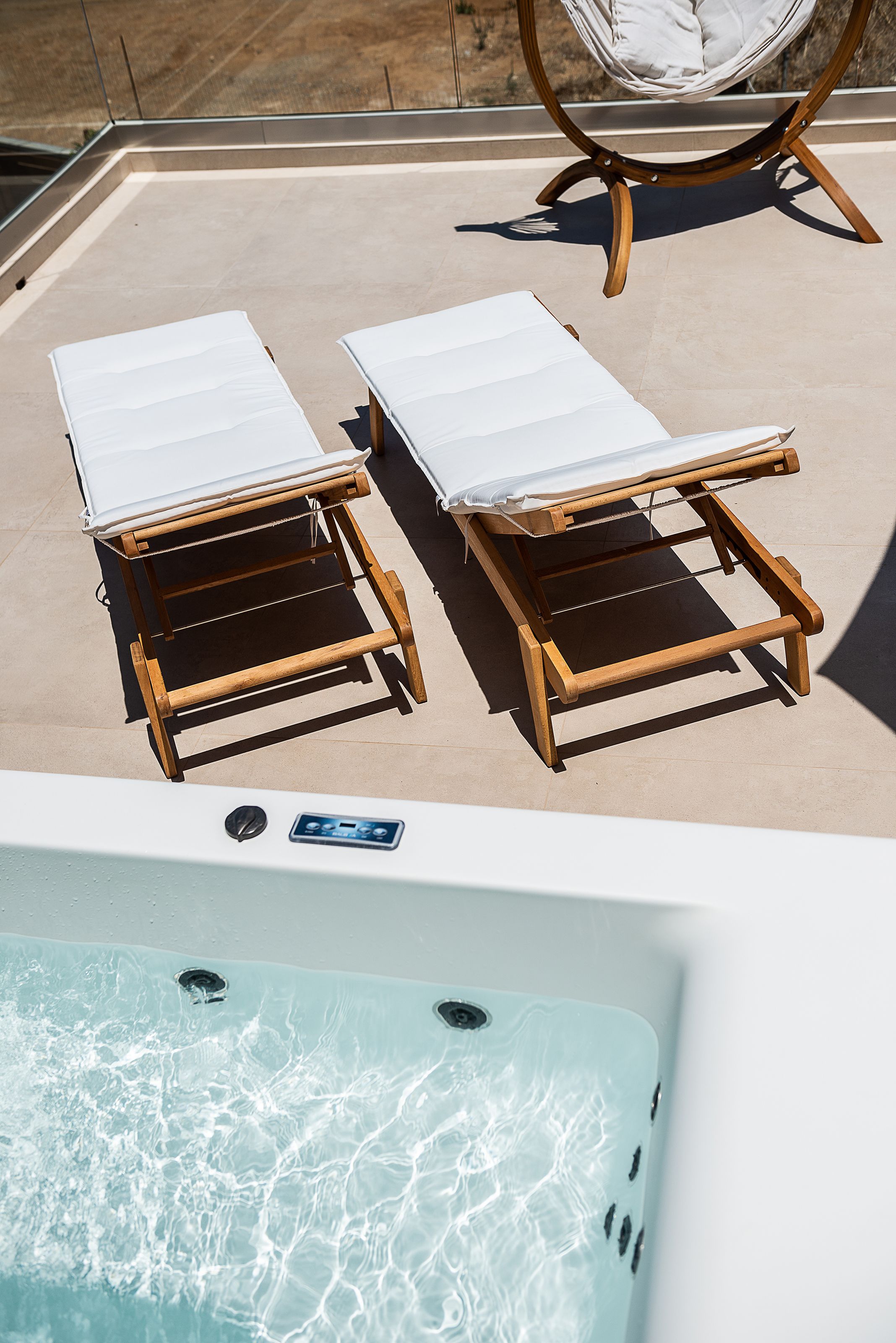 Two wooden lounge chairs with white cushions, a wooden table, and a hot tub with clear water.