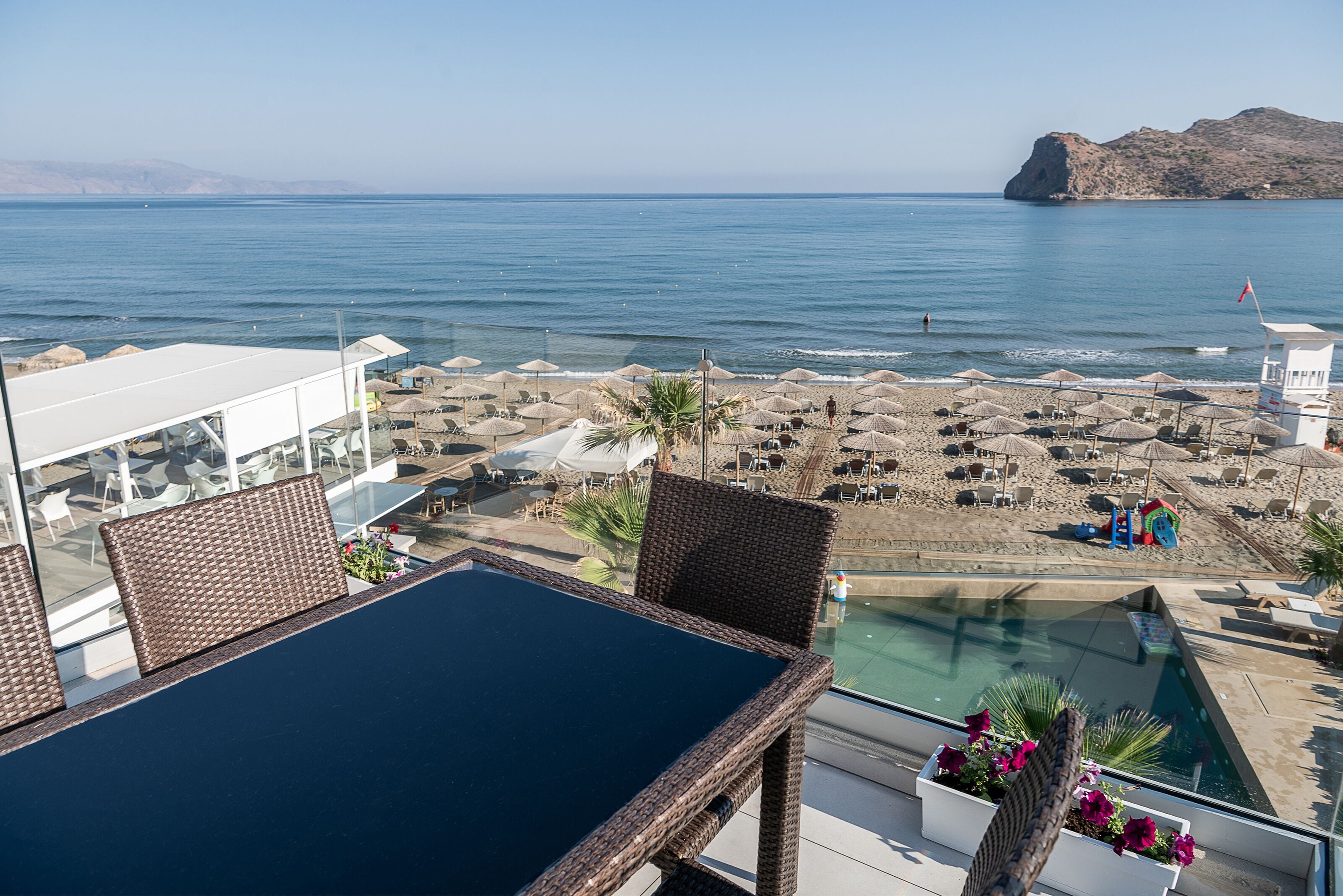 Una terraza con mobiliario de mimbre, piscina y vista a la playa y al mar.