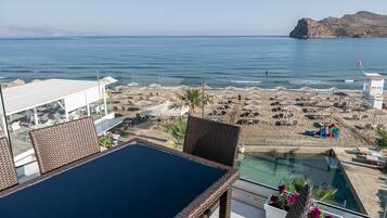 Una terraza con mobiliario de mimbre, piscina y vista a la playa y al mar.