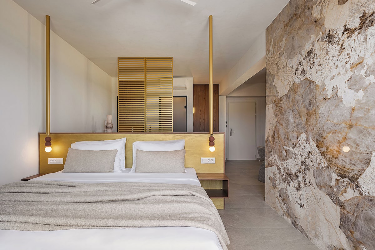 A modern bedroom with a large bed, wooden headboard, and a stone accent wall.