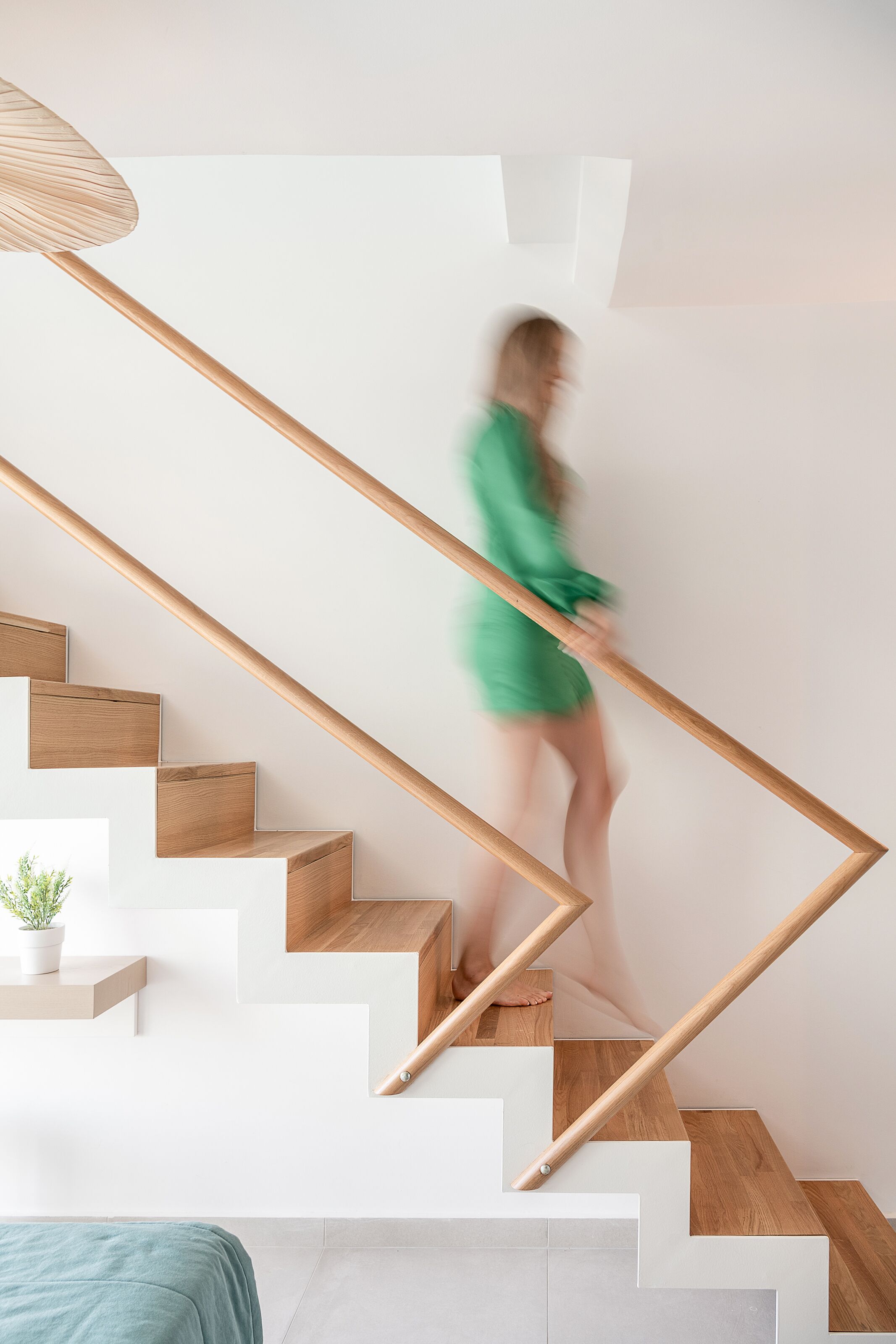 A modern staircase with wooden steps and a wooden handrail, leading to a landing with a potted plant.