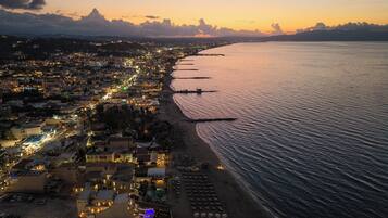 An aerial view of a coastal town at sunset with a beach, boats, and a marina.