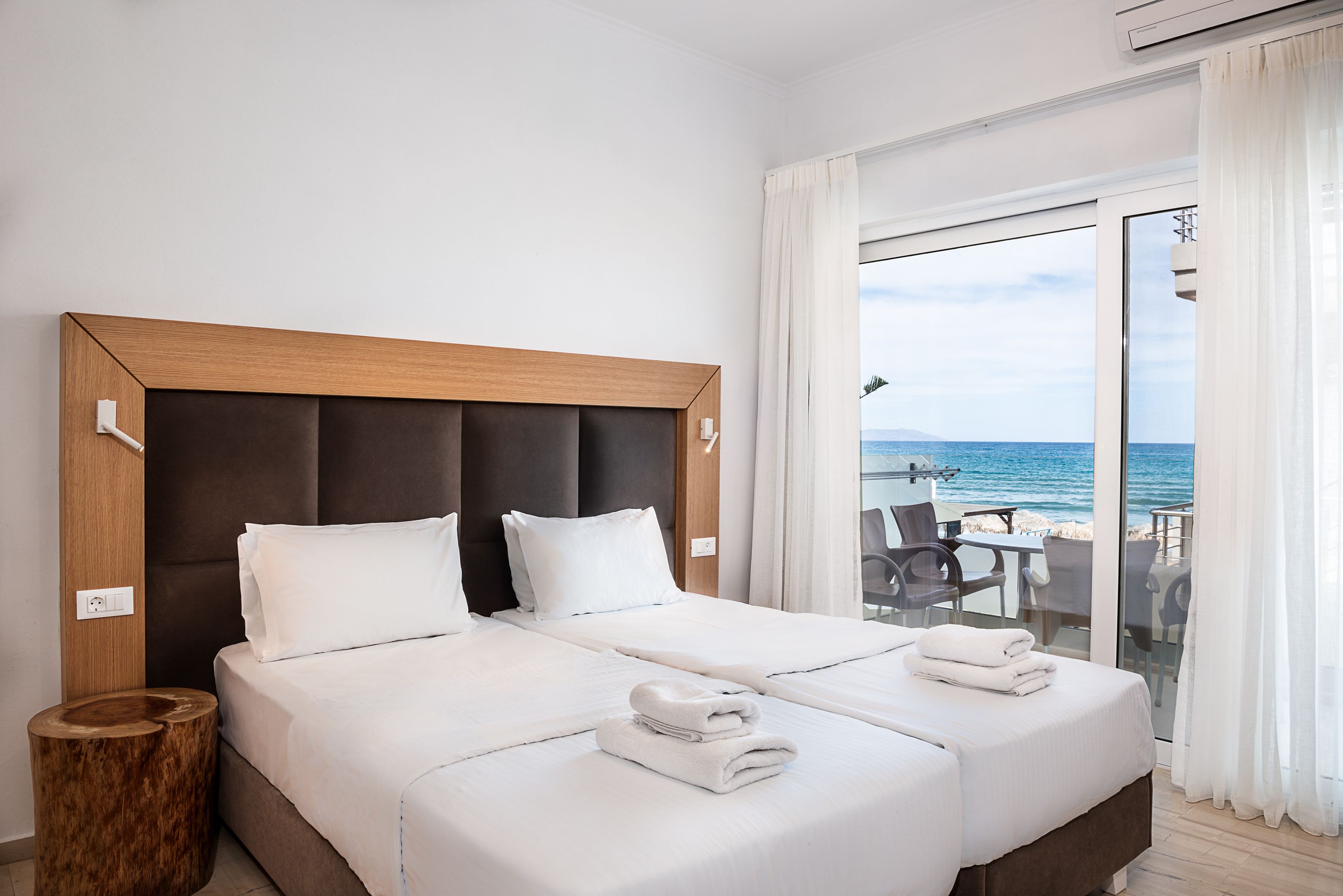 Een hotelkamer met een groot bed, een houten hoofdeinde en uitzicht op het strand door een glazen deur.