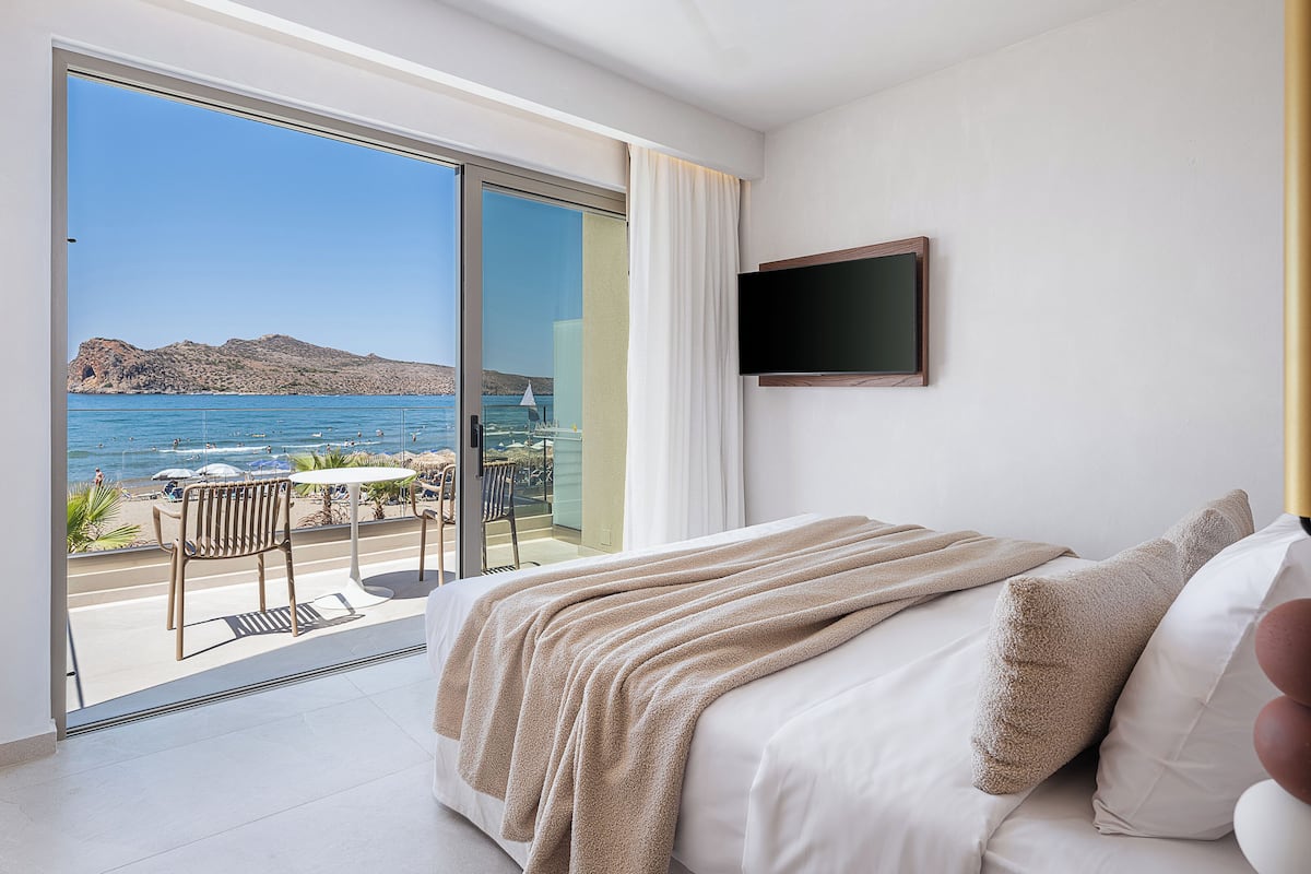A bedroom with a bed, a TV, and a balcony with a view of the sea.