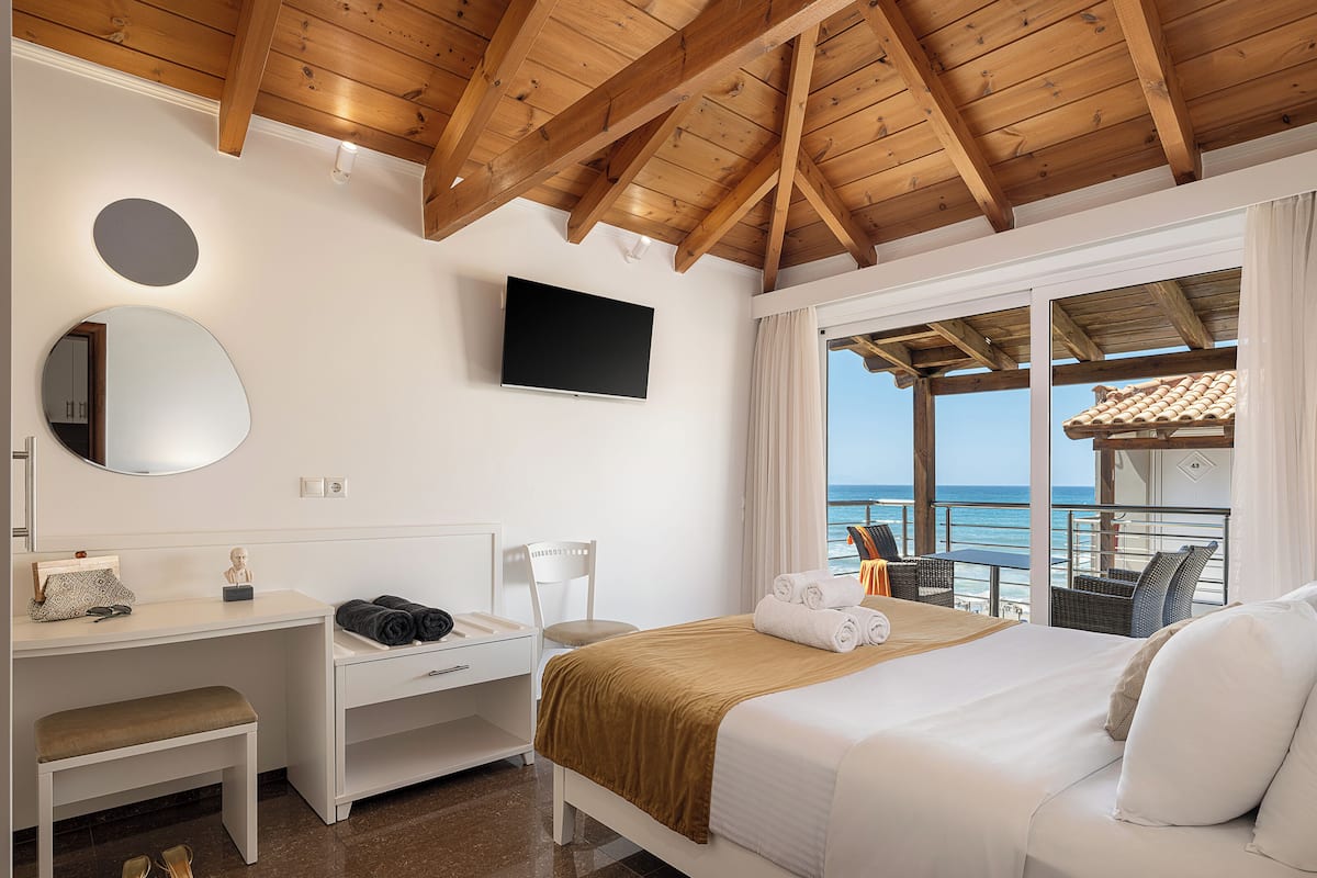 A hotel room with a bed, a desk, a chair, a TV, and a view of the sea.