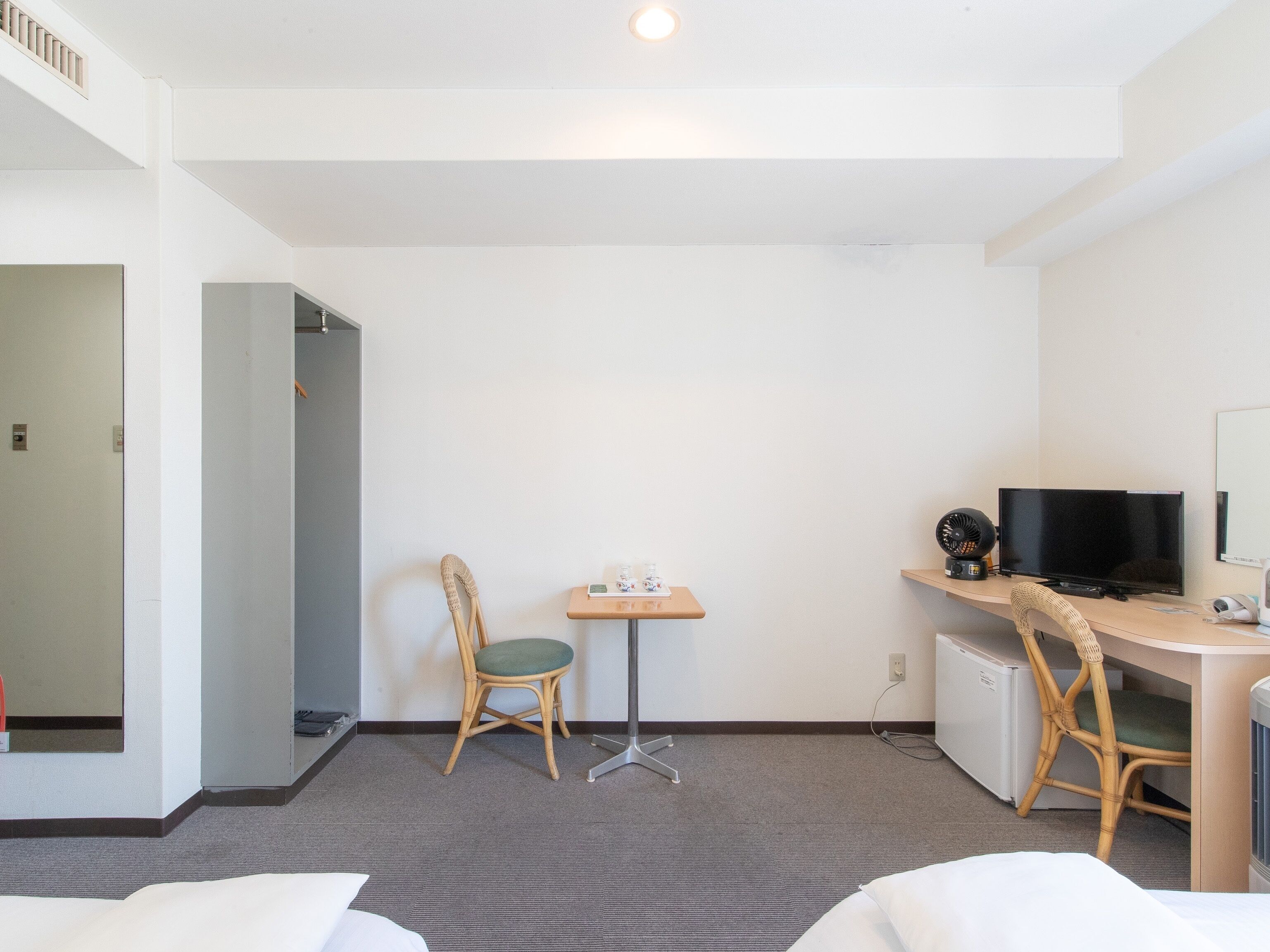 Ein Hotelzimmer mit Bett, Schreibtisch mit Computer und Fernseher, Stuhl und kleiner Tisch mit Telefon und Tasse.