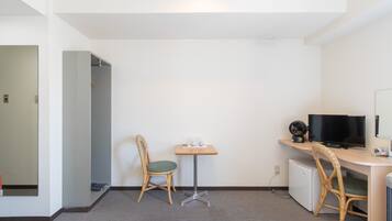 Ein Hotelzimmer mit Bett, Schreibtisch mit Computer und Fernseher, Stuhl und kleiner Tisch mit Telefon und Tasse.