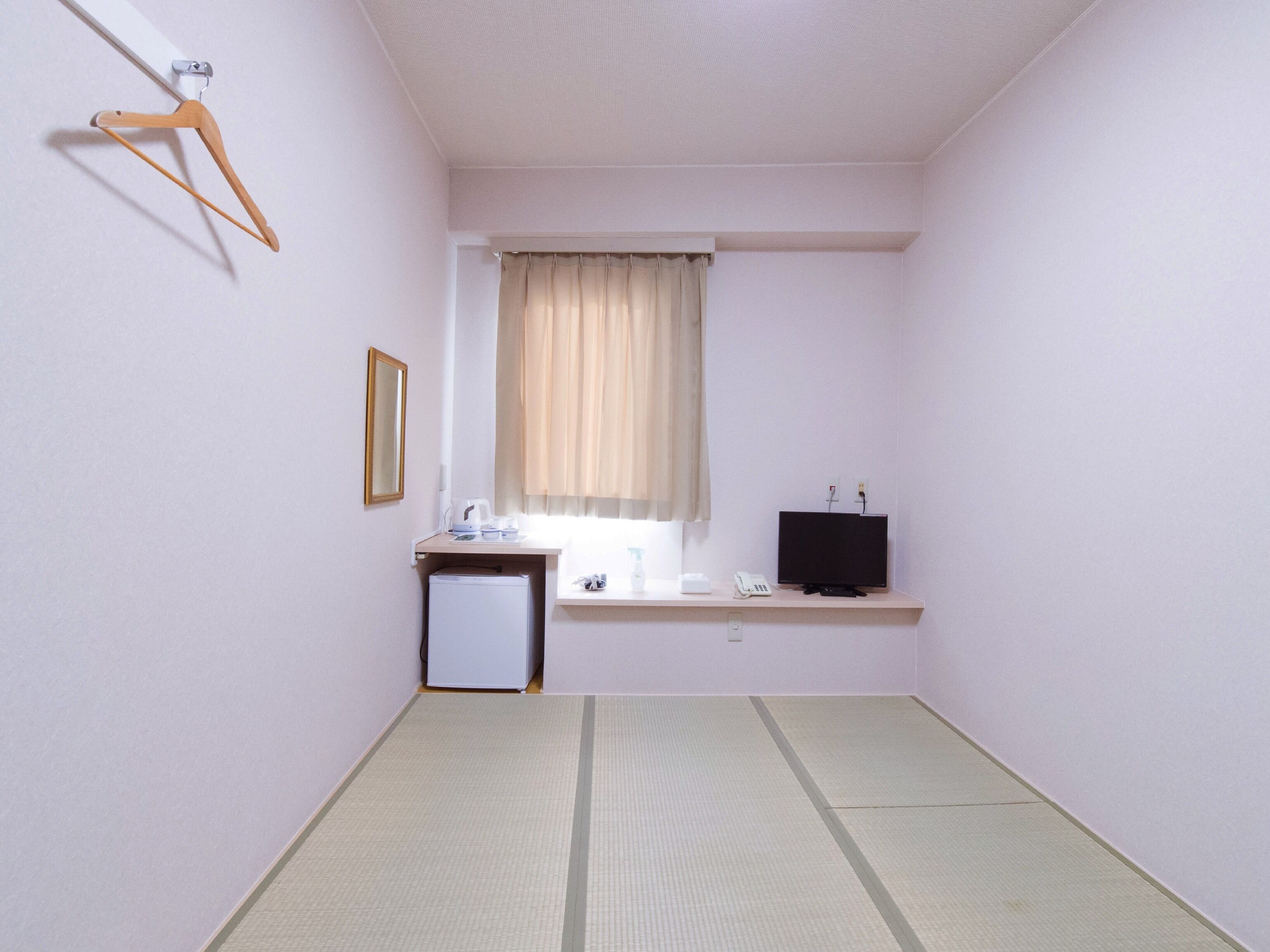 A small, clean room with a bed, a bedside table, a TV, and a window with curtains.