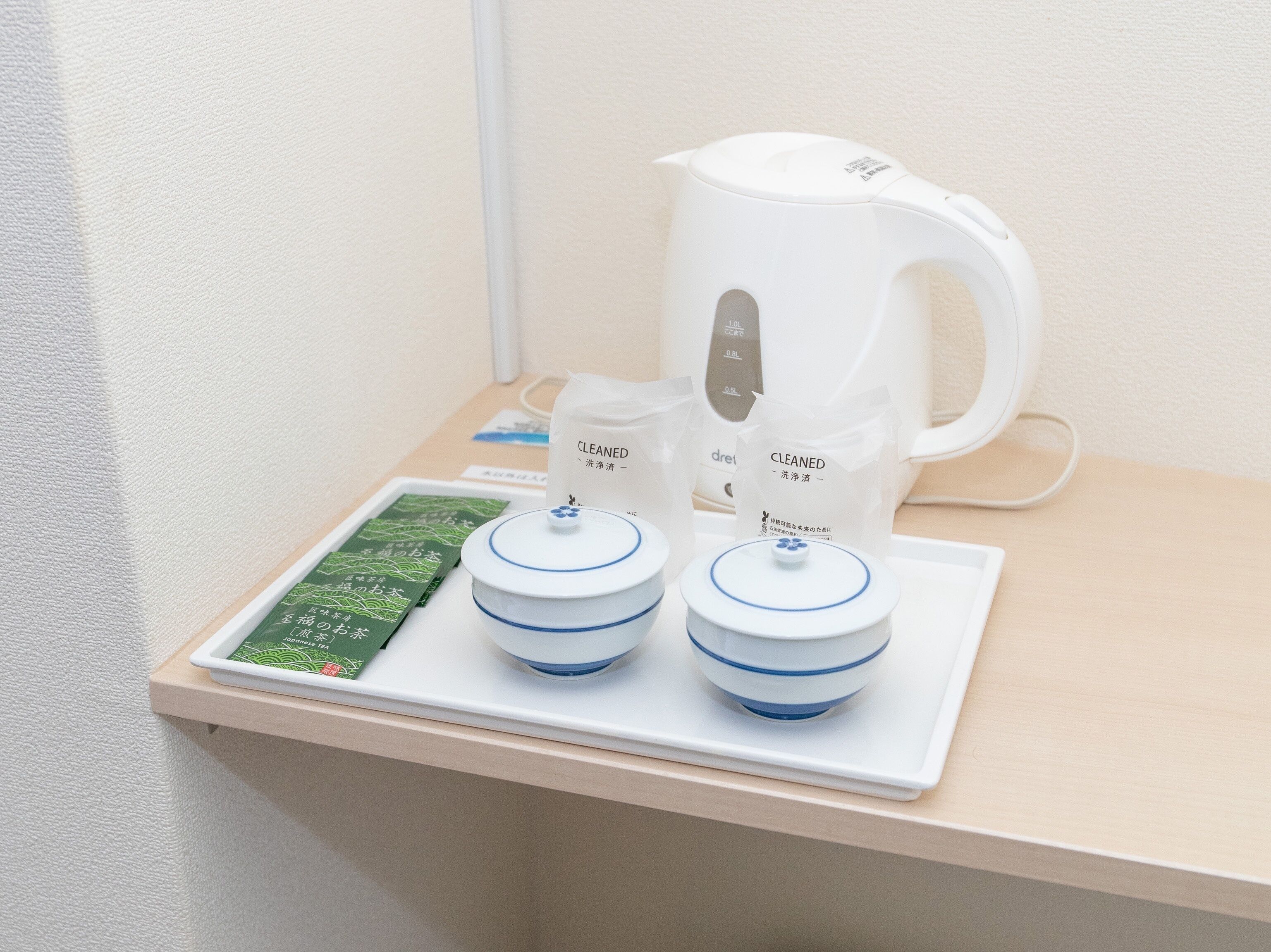A clean, modern bathroom with a white sink, a white electric kettle, and two containers labeled "CLEANED" on a wooden countertop.