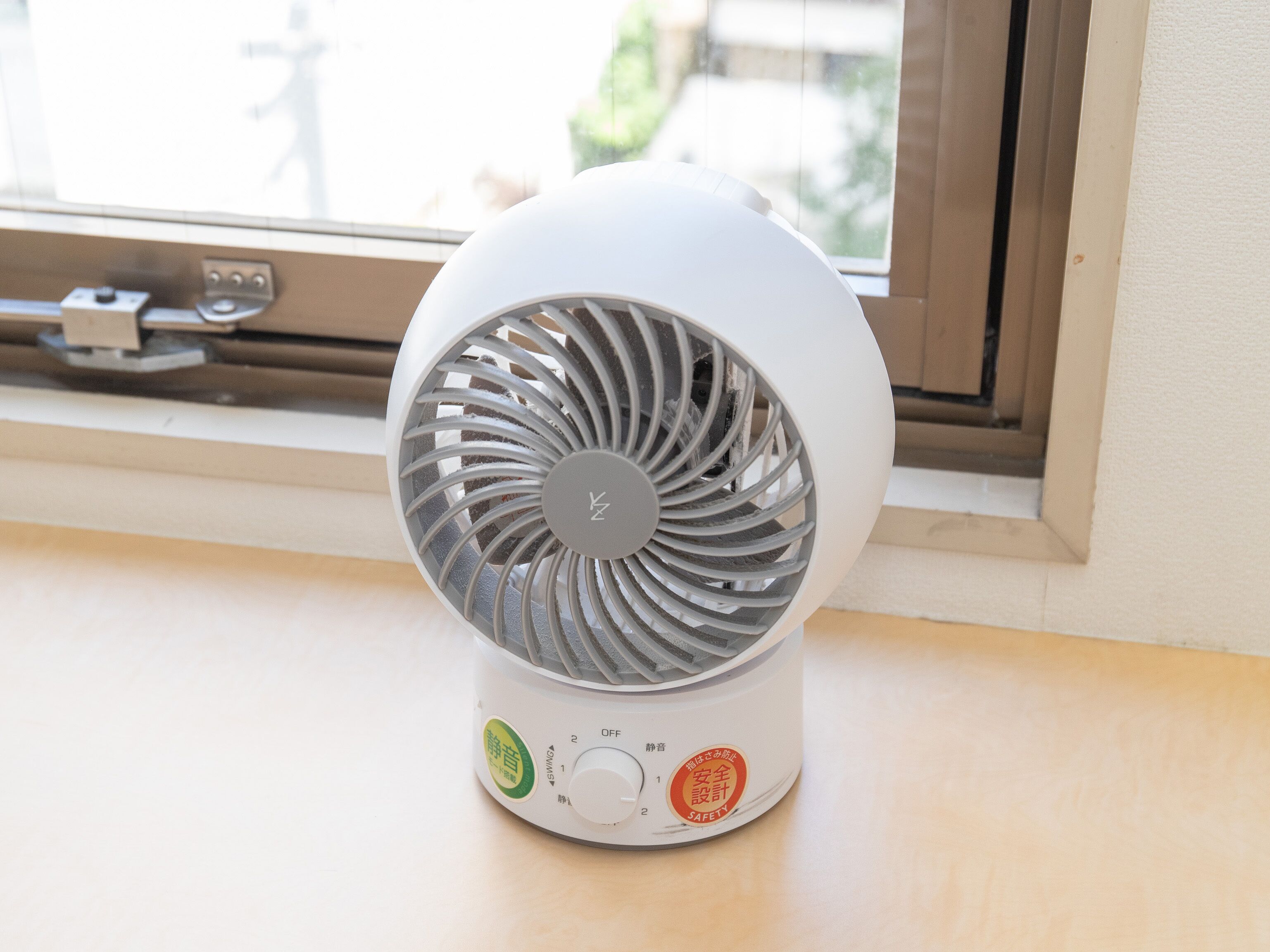 Un ventilateur portatif blanc, doté d’un panneau de commande et d’étiquettes de certification de sécurité, est posé sur un rebord de fenêtre.