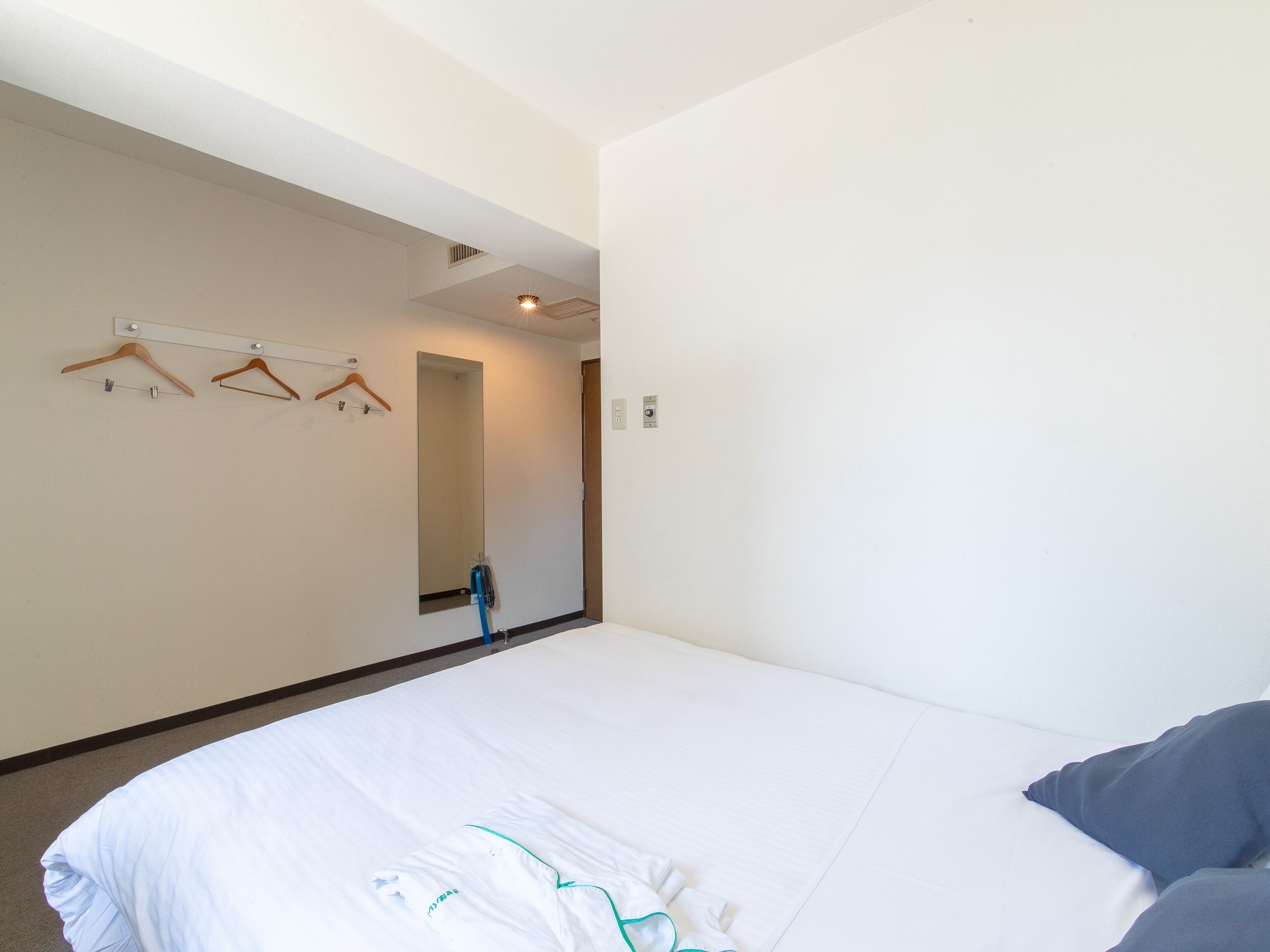 A hotel room with a large bed, a mirror, and wooden hangers on the wall.