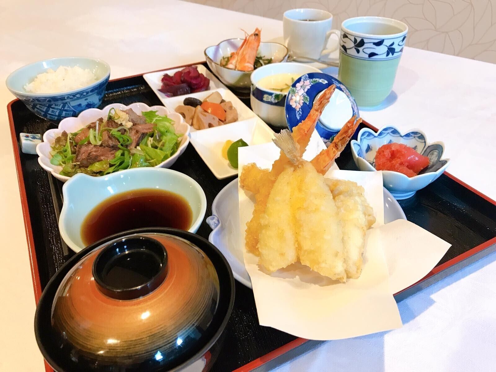 A tray with various Japanese dishes including tempura, sashimi, and rice.