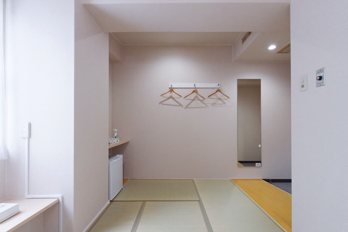 Une pièce avec un sol recouvert de tatamis, une petite armoire blanche et un miroir au mur.