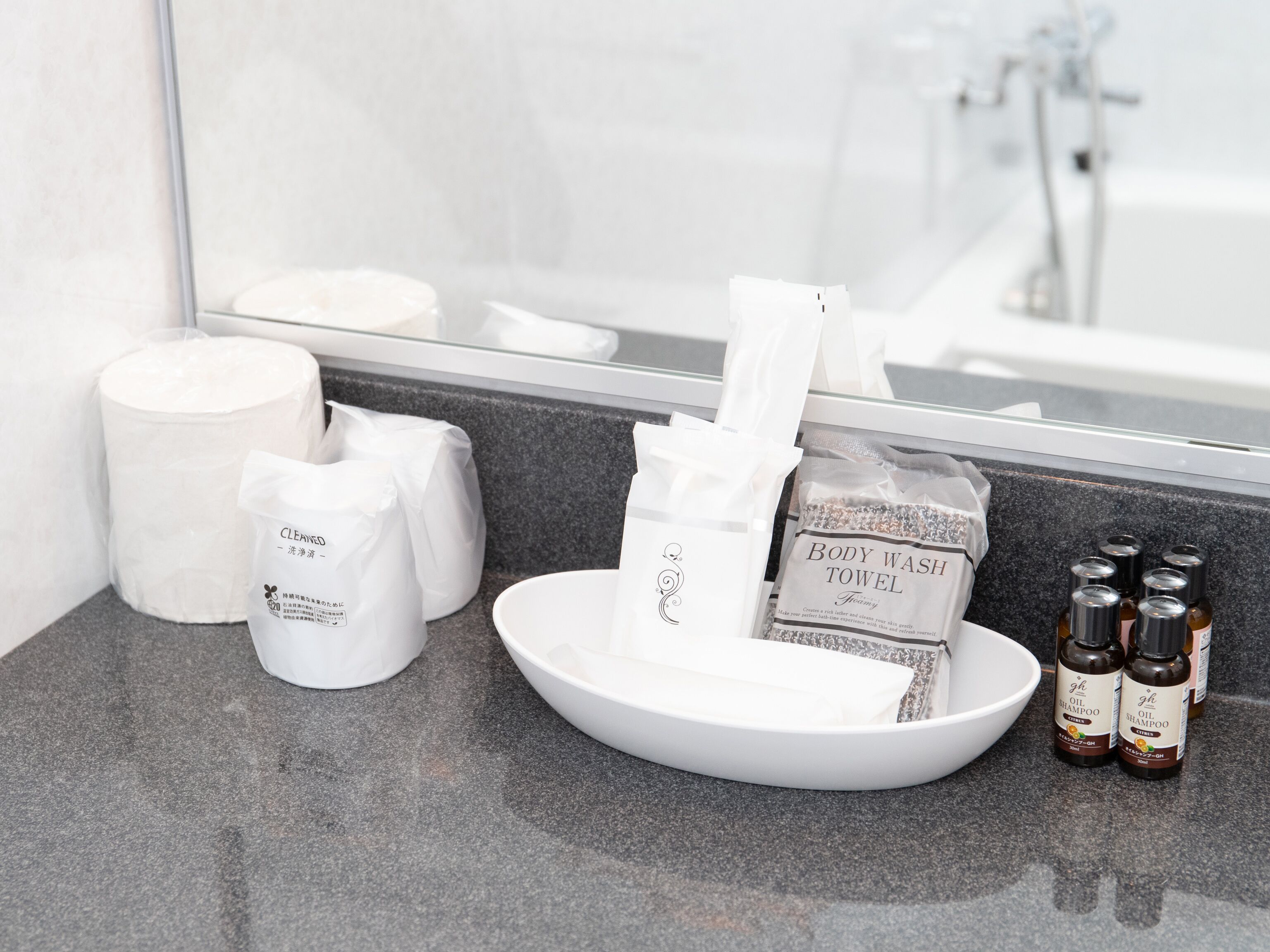 Un meuble-lavabo de salle de bain avec un lavabo blanc, un miroir et des articles de toilette, notamment une serviette pour le corps, un nettoyant pour le visage et deux flacons de shampoing.