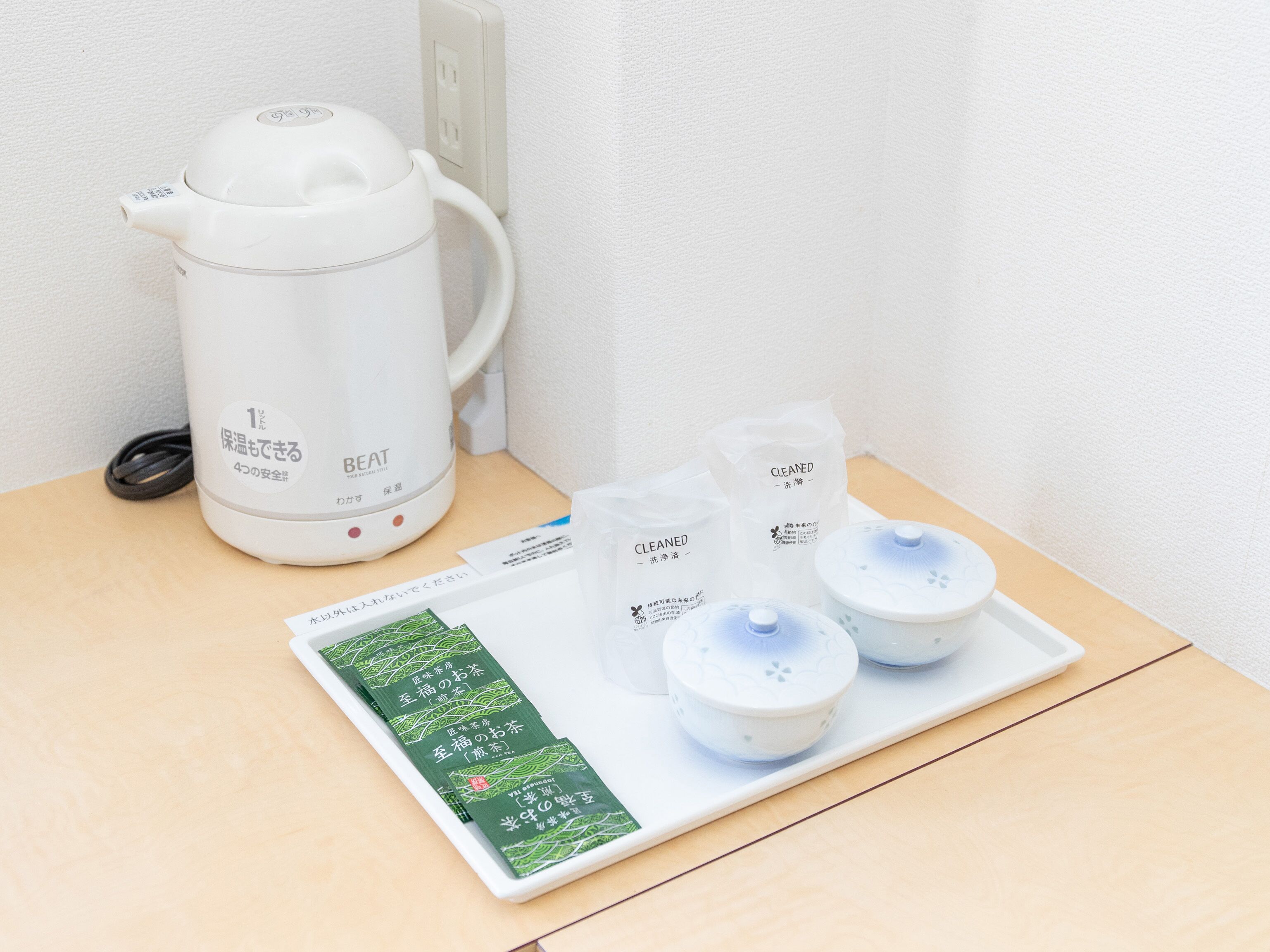 Une bouilloire électrique blanche, une assiette avec des sachets de thé et un plateau avec des tasses à thé, le tout posé sur une table en bois.