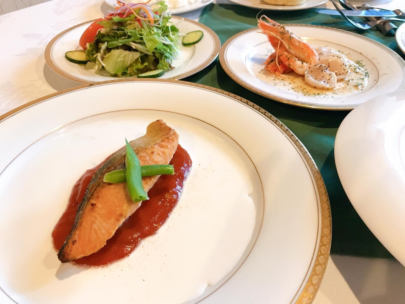 Une table à manger avec des assiettes remplies de nourriture, notamment un plat de poisson accompagné de haricots verts et un plat de crevettes.