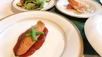 Une table à manger avec des assiettes remplies de nourriture, notamment un plat de poisson accompagné de haricots verts et un plat de crevettes.