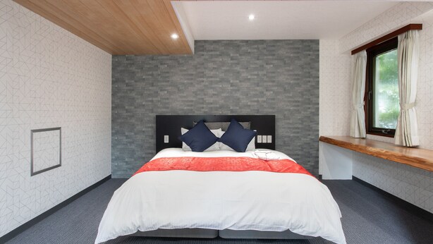 Een moderne slaapkamer met een houten plafond, een grijze bakstenen muur, en een groot bed met een wit en rode spreidekker.