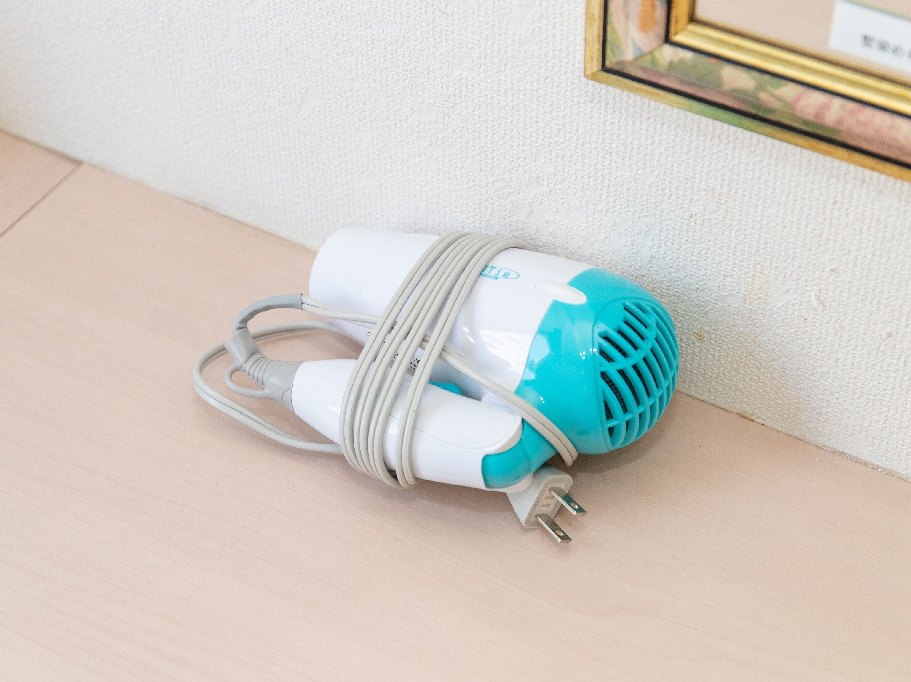 A white and blue portable speaker with a coiled cable, placed on a wooden surface against a textured wall.