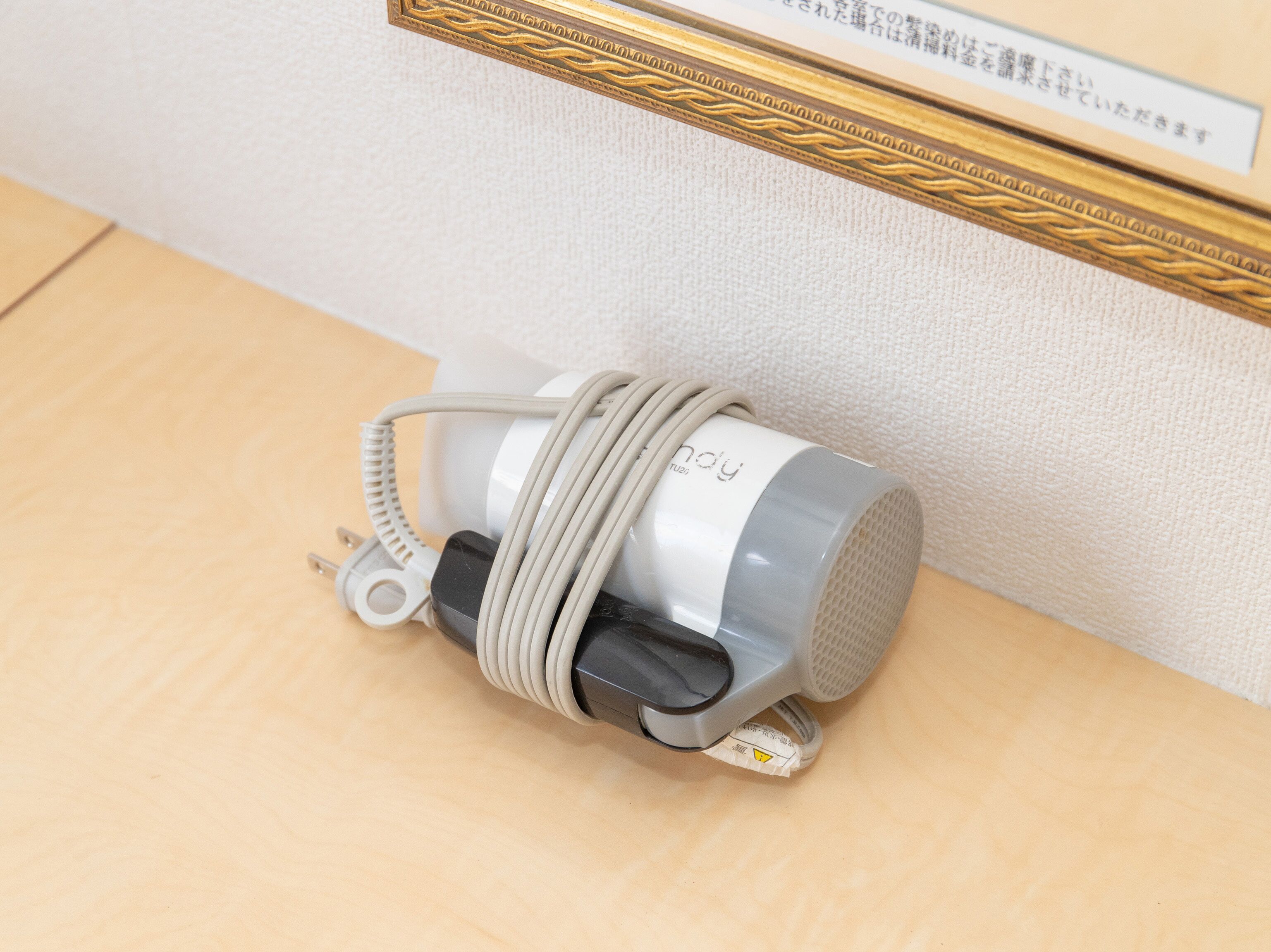 A small, gray, cylindrical device with a coiled cable, possibly a portable speaker, on a wooden surface.
