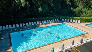A rectangular swimming pool with multiple lanes, surrounded by white lounge chairs and umbrellas, set against a backdrop of dense greenery. - Residence Il Paradiso (Guardistallo)