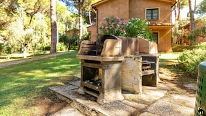 A stone barbecue grill in a garden with a house in the background. - Residence Il Paradiso (Guardistallo)