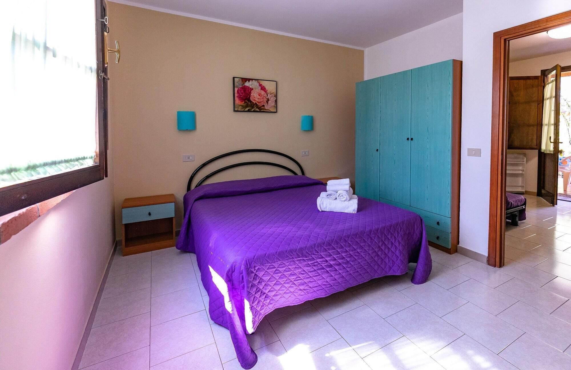 A bedroom with a bed, a wardrobe, a nightstand, and a painting on the wall.
