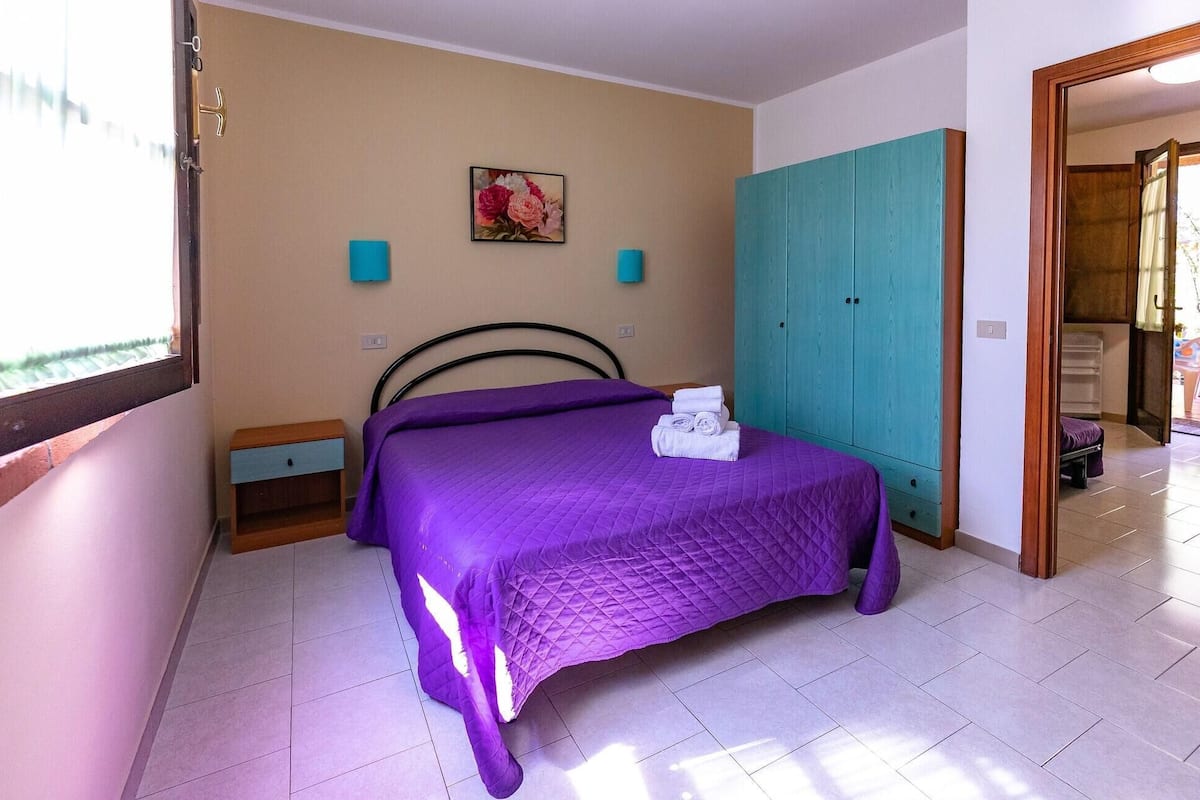 Un dormitorio con cama, armario, mesita de noche y un cuadro en la pared.