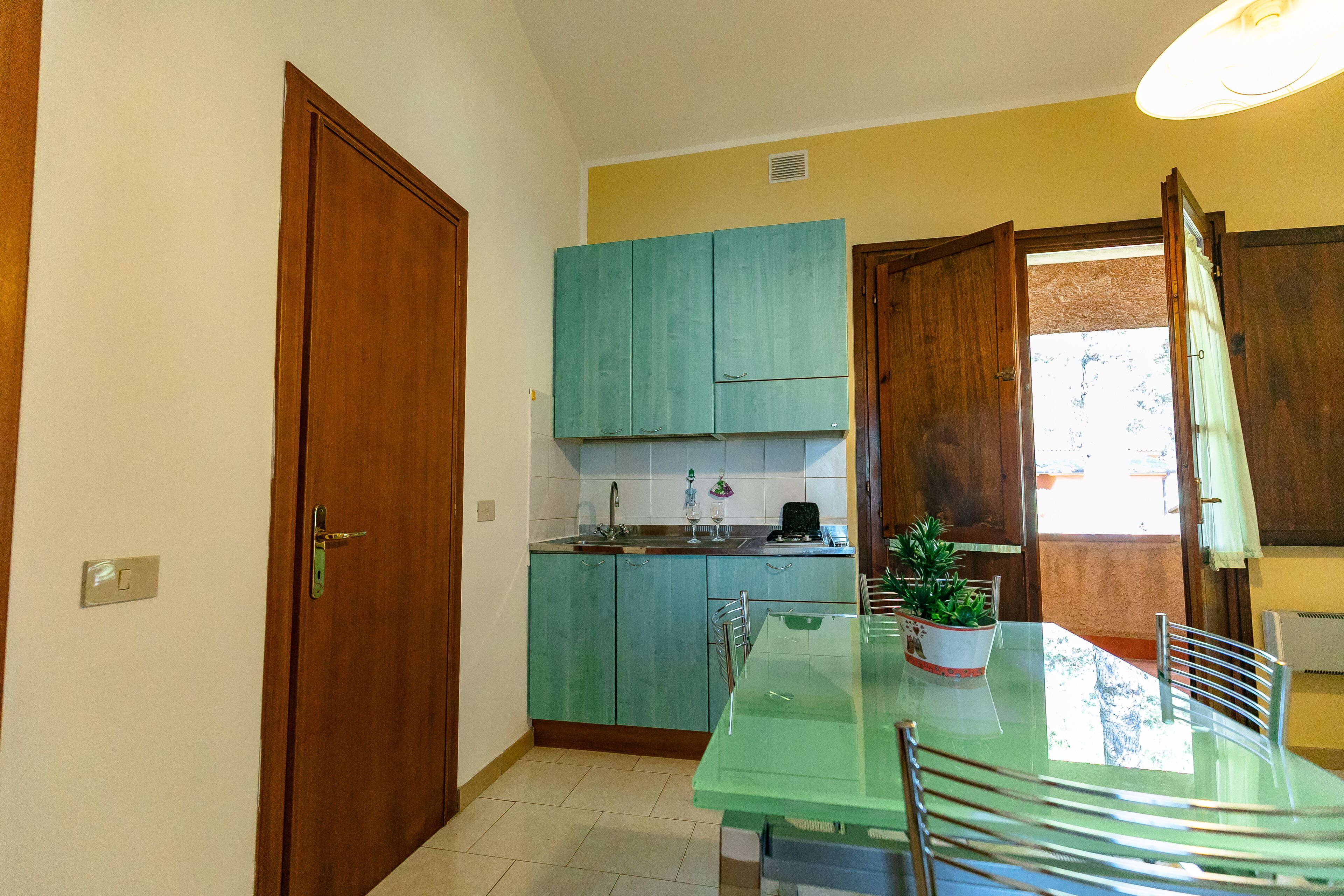 Una cocina compacta con armarios color turquesa, una mesa de comedor de vidrio y una planta en maceta.
