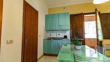 Una cocina compacta con armarios color turquesa, una mesa de comedor de vidrio y una planta en maceta.