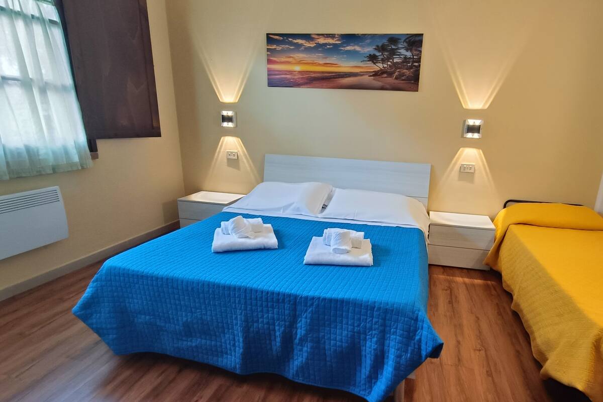 Habitación de hotel con cama, mesita de noche, cortinas y un cuadro en la pared.