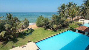 A swimming pool with a view of the ocean, surrounded by palm trees and a grassy area. - Serendib Beach Resort (Induruwa)