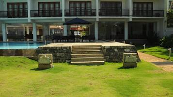 A hotel with a swimming pool, outdoor seating, and a stone staircase leading to the entrance.