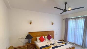 A hotel room with a wooden bed, a ceiling fan, a bedside table with a lamp, and a window with curtains.