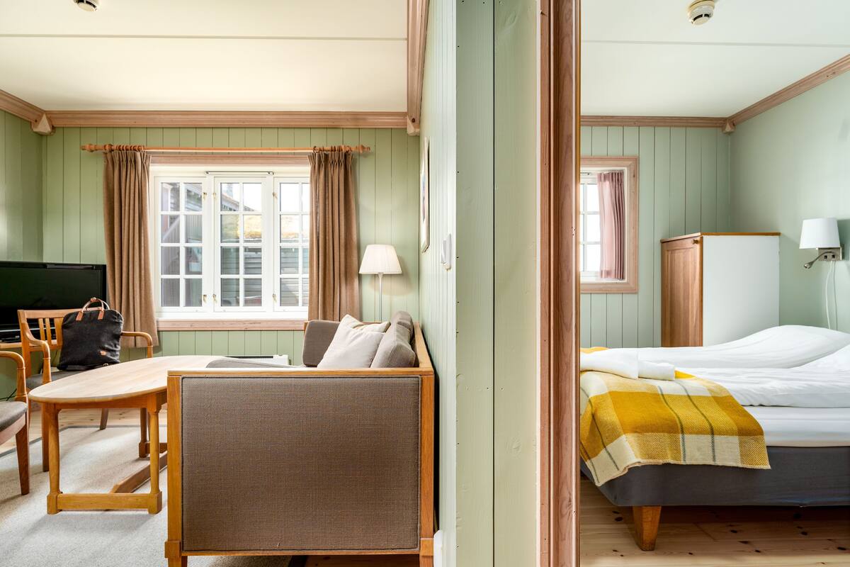 A room with a bed, a desk, a chair, a television, and a window with curtains.