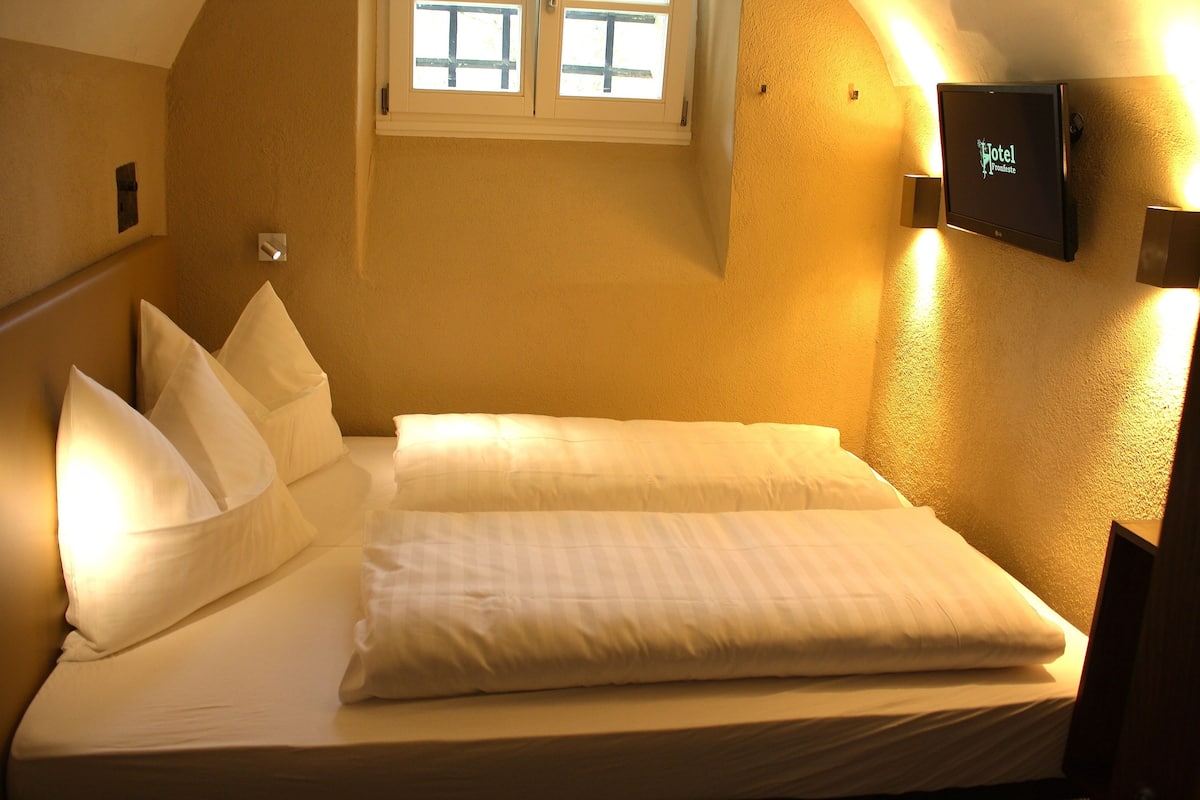 Una habitación de hotel con una cama bien hecha, un televisor montado y una ventana con persianas.