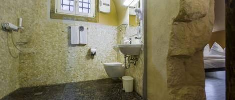 A bathroom with a stone mosaic wall, a shower, a toilet, and a sink.