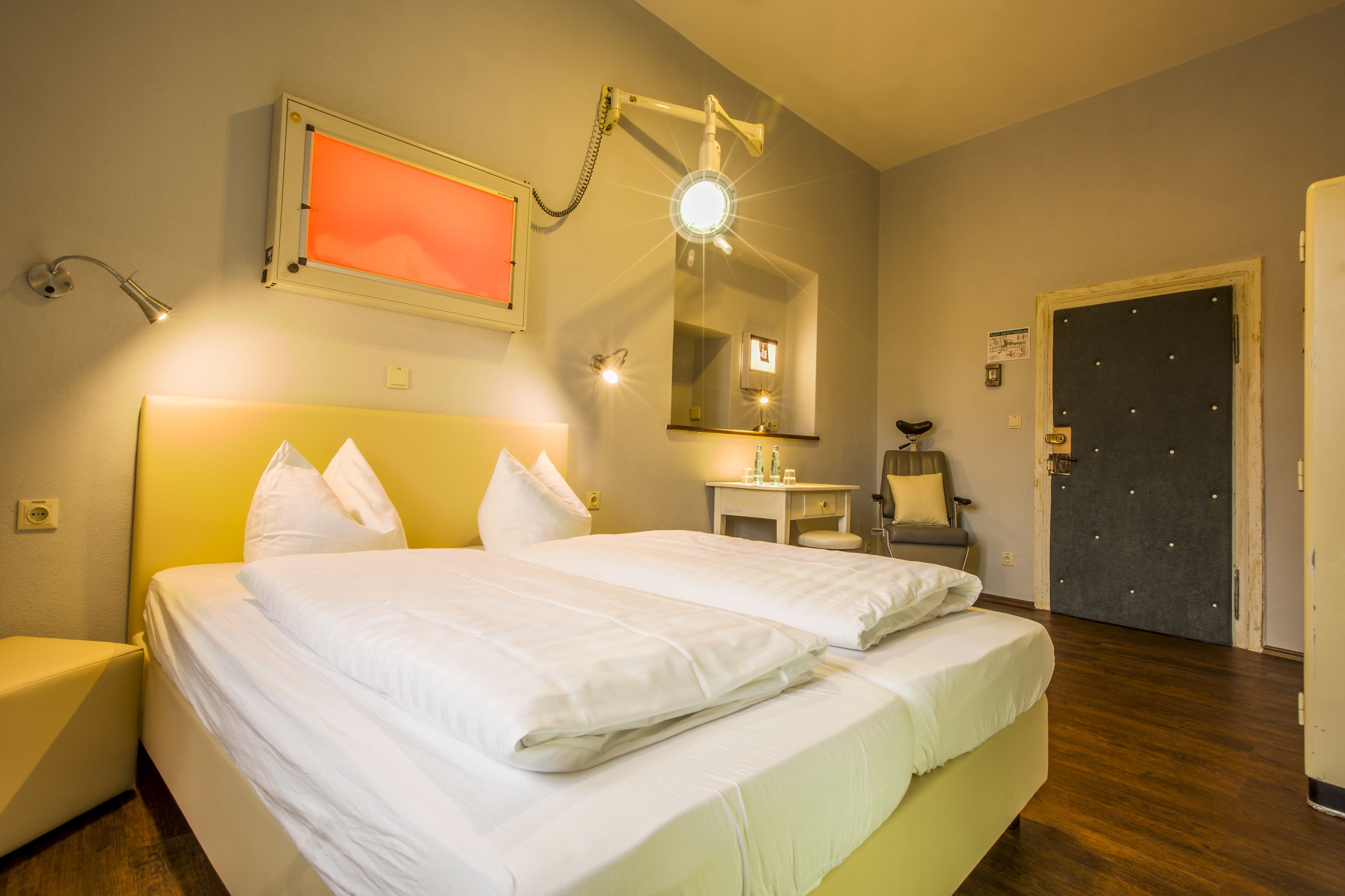 A hotel room with a double bed, bedside tables, a chair, a desk, a mirror, and a door.