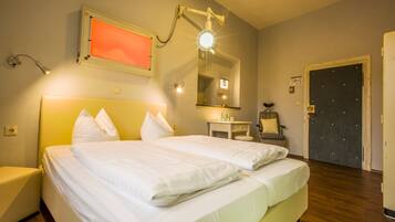 Ein Hotelzimmer mit Doppelbett, Nachttischen, einem Sessel, einem Schreibtisch, einem Spiegel und einer Tür.