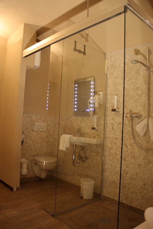A glass-enclosed shower with a handheld showerhead, a handheld dryer, and a towel rack.