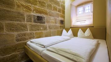 A room with a stone wall, a bed with white bedding, and a window above the bed.