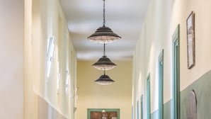 Un pasillo con suelo de madera, puertas verdes e iluminación colgante.
