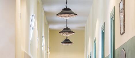 Un pasillo con suelo de madera, puertas verdes e iluminación colgante.