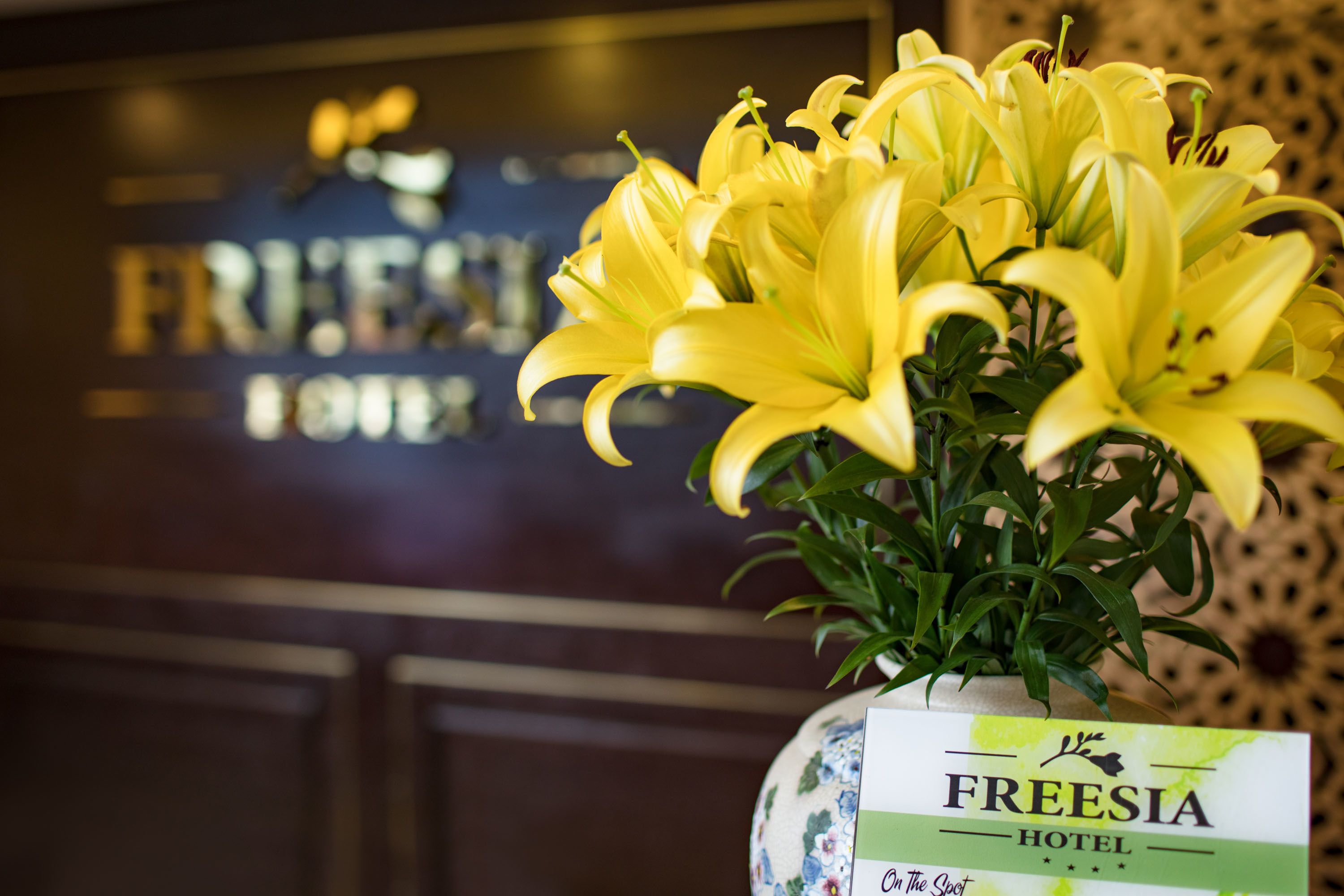 A vase with yellow lilies placed on a table in a hotel lobby.